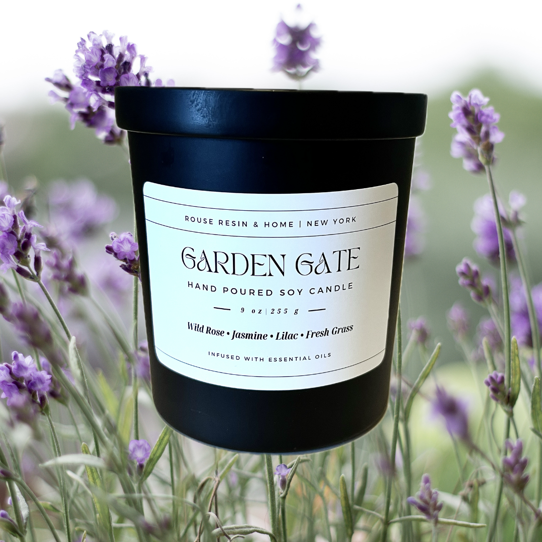 A black candle jar with purple flowers in the background.