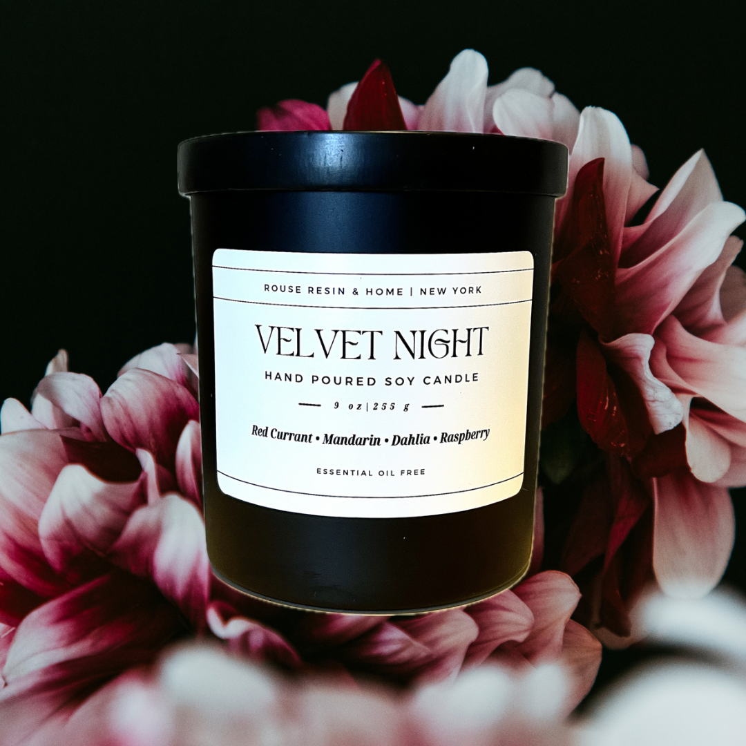 A black candle jar with pink and white flowers in the background.